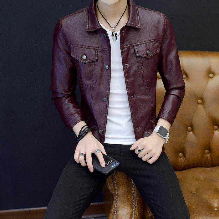 Men's burgundy motorcycle leather jacket styled with white shirt and black pants sitting on a brown leather sofa